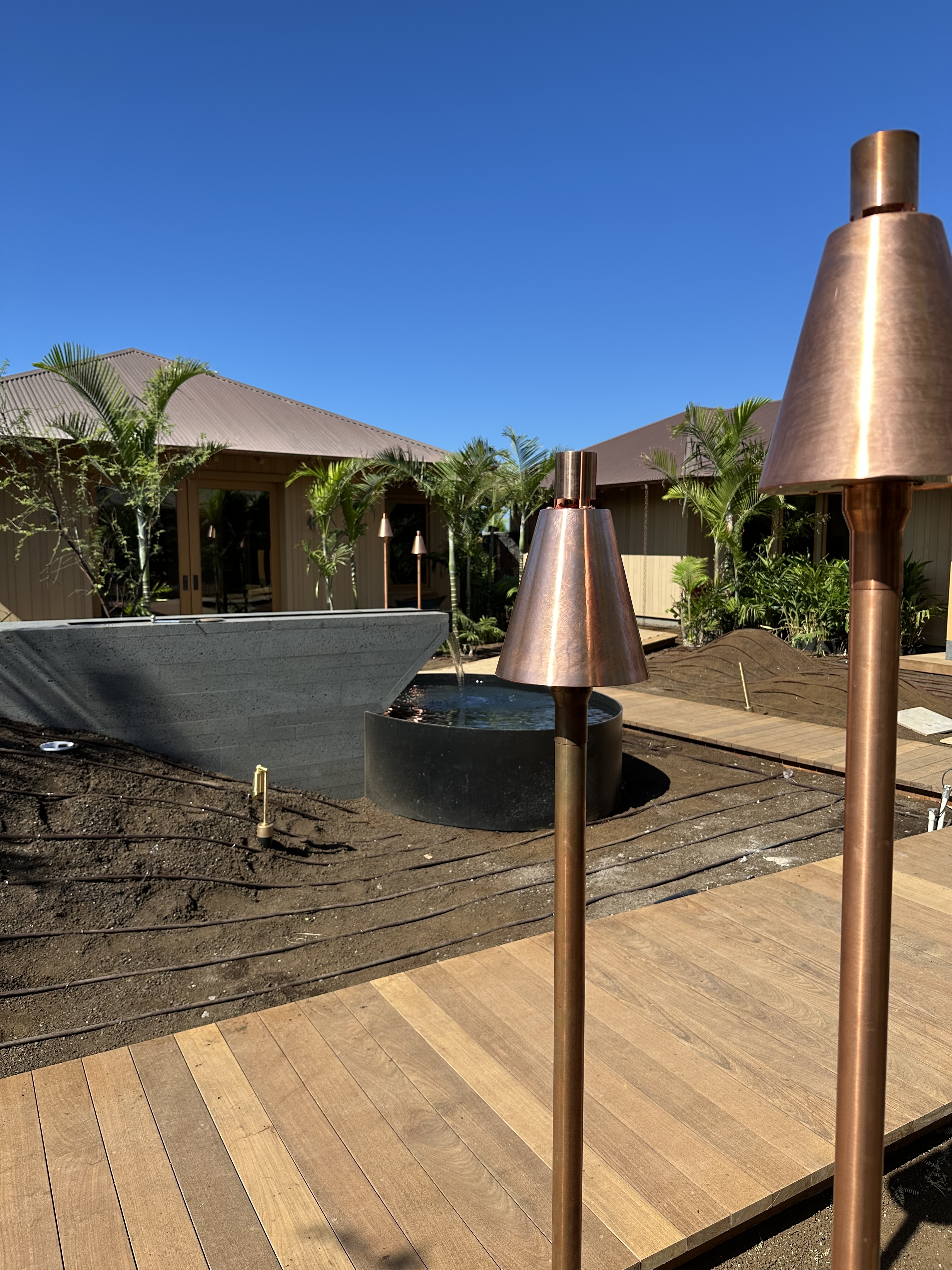 Crossed KAZ tiki torches installed in lava rock with palm trees and Pacific horizon