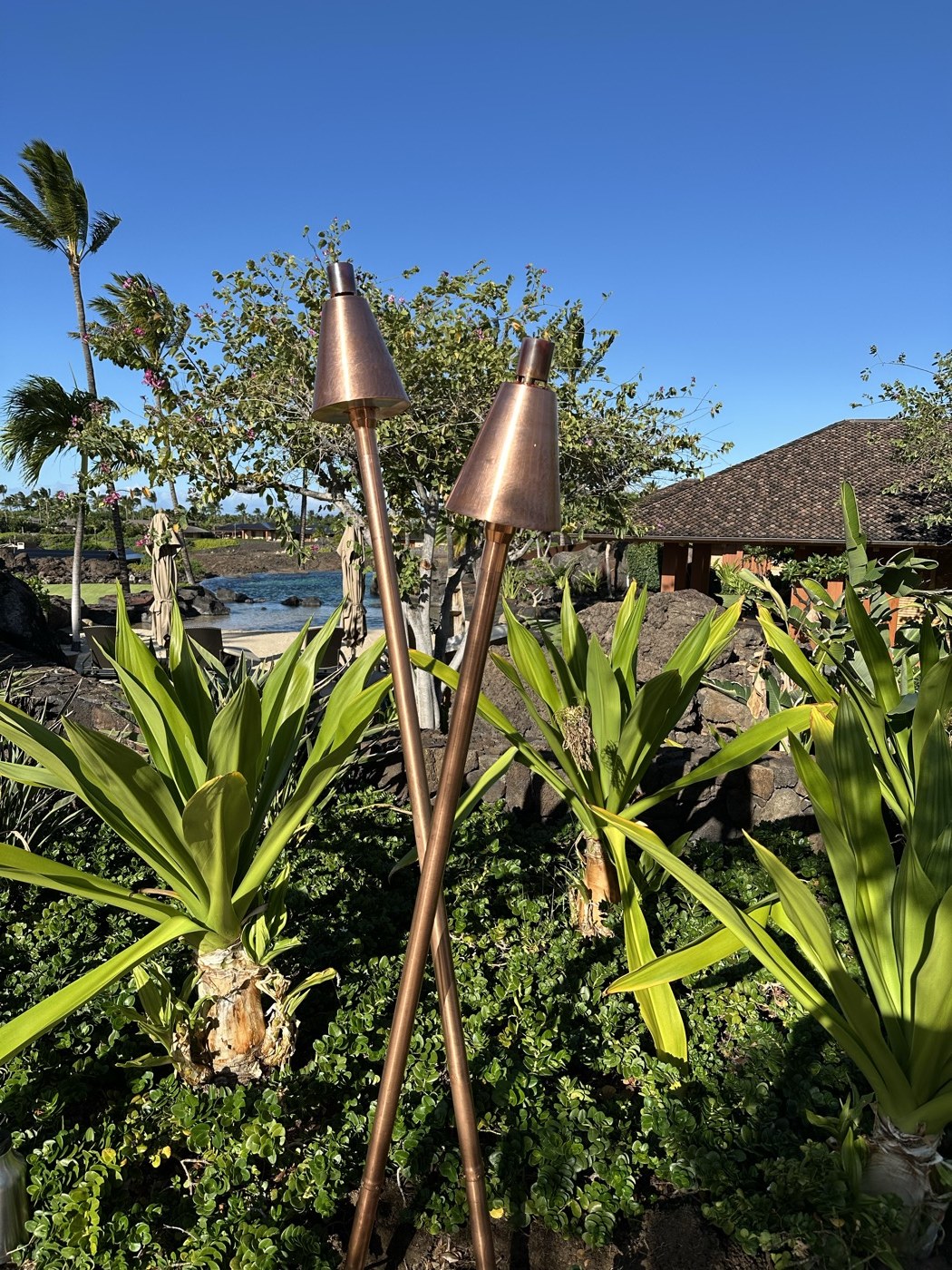 Close-up of copper KAZ tiki torch with tropical garden backdrop
